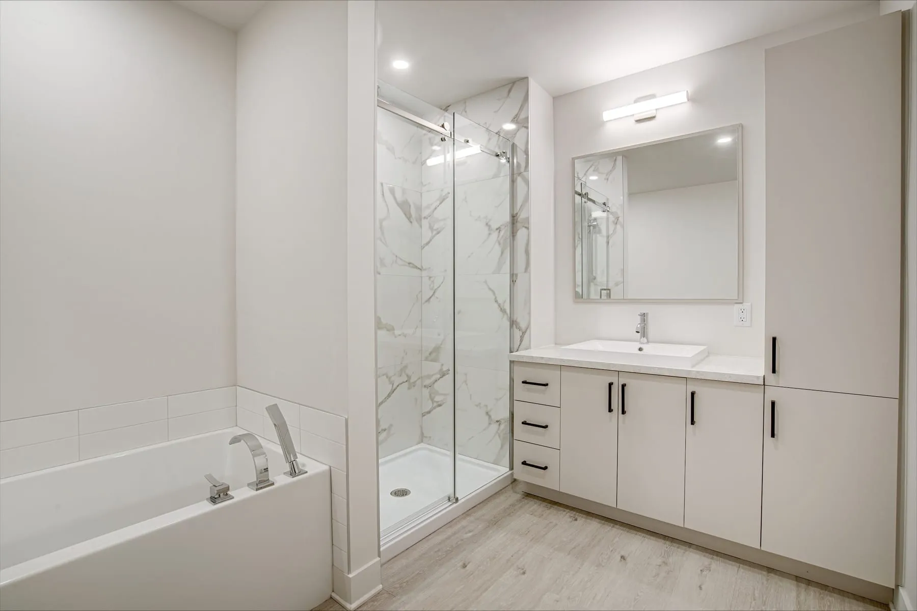 Salle de bain avec bain et douche vitrée séparés, céramique marbrée et vanité claire